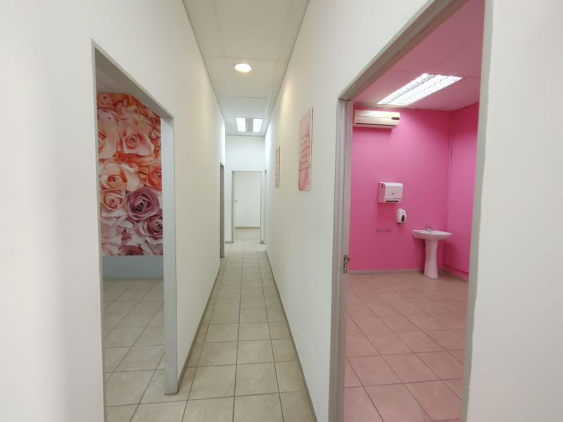 A commercial hallway providing access to multiple rooms, including a washroom area featuring a pedestal sink and wall-mounted air conditioning unit.