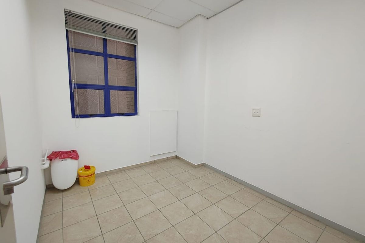 A clean, empty commercial bathroom space featuring tiled flooring, a suspended ceiling, and a blue-framed window providing natural light.