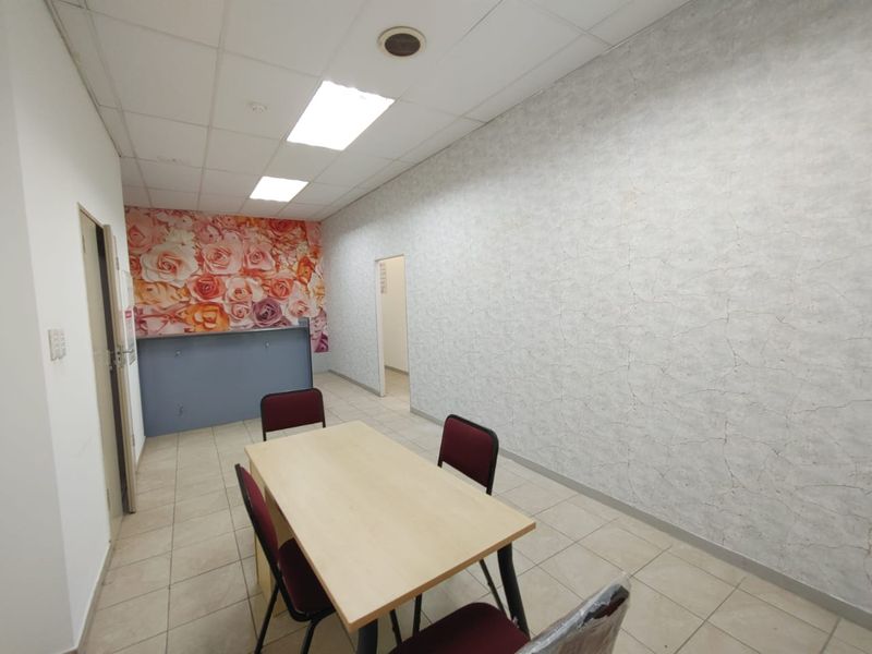 A functional office space featuring ceramic floor tiles, a suspended ceiling with recessed lighting, and a built-in reception counter with decorative floral wall accents.