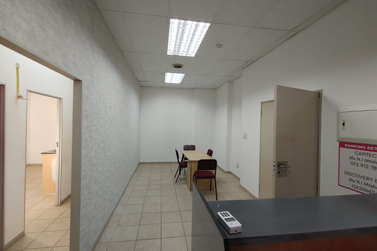A functional commercial office space featuring tiled flooring, a built-in reception counter, and recessed ceiling lighting, suitable for professional use.
