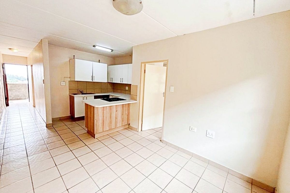 Open-plan living and kitchen area featuring tiled flooring, built-in cabinetry, and a functional hob, offering a blank canvas for potential renovation.