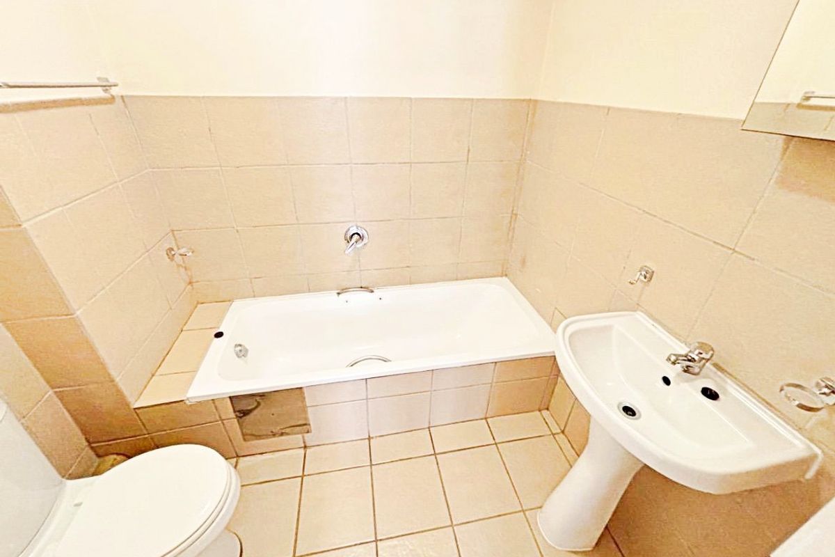 A dated bathroom featuring a standard bathtub, pedestal basin, and toilet with neutral wall and floor tiling.