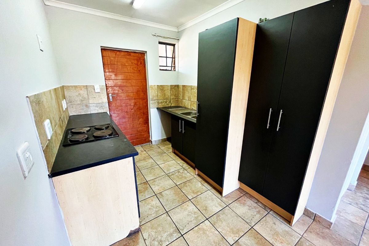 A functional kitchen featuring dark cabinetry, a built-in electric hob, double sink, and tiled flooring with a neutral backsplash.
