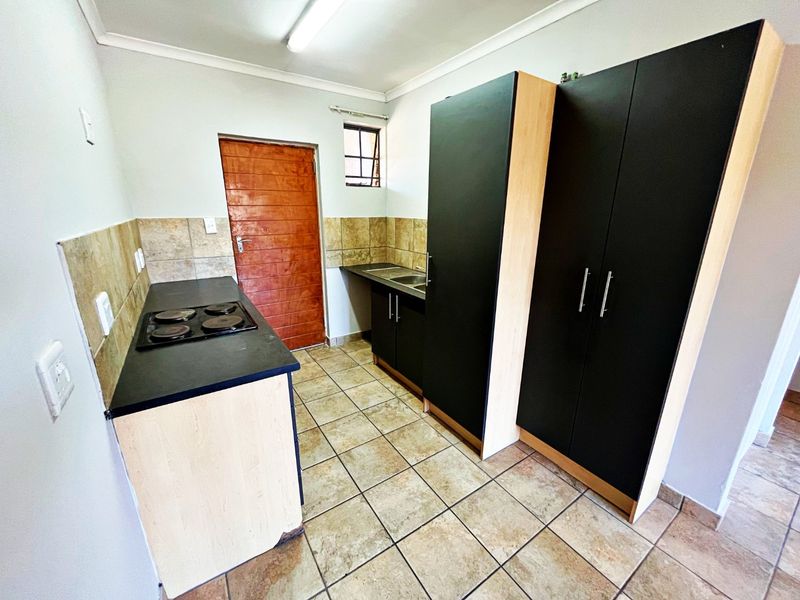 A functional kitchen featuring dark cabinetry, a built-in electric hob, double sink, and tiled flooring with a neutral backsplash.
