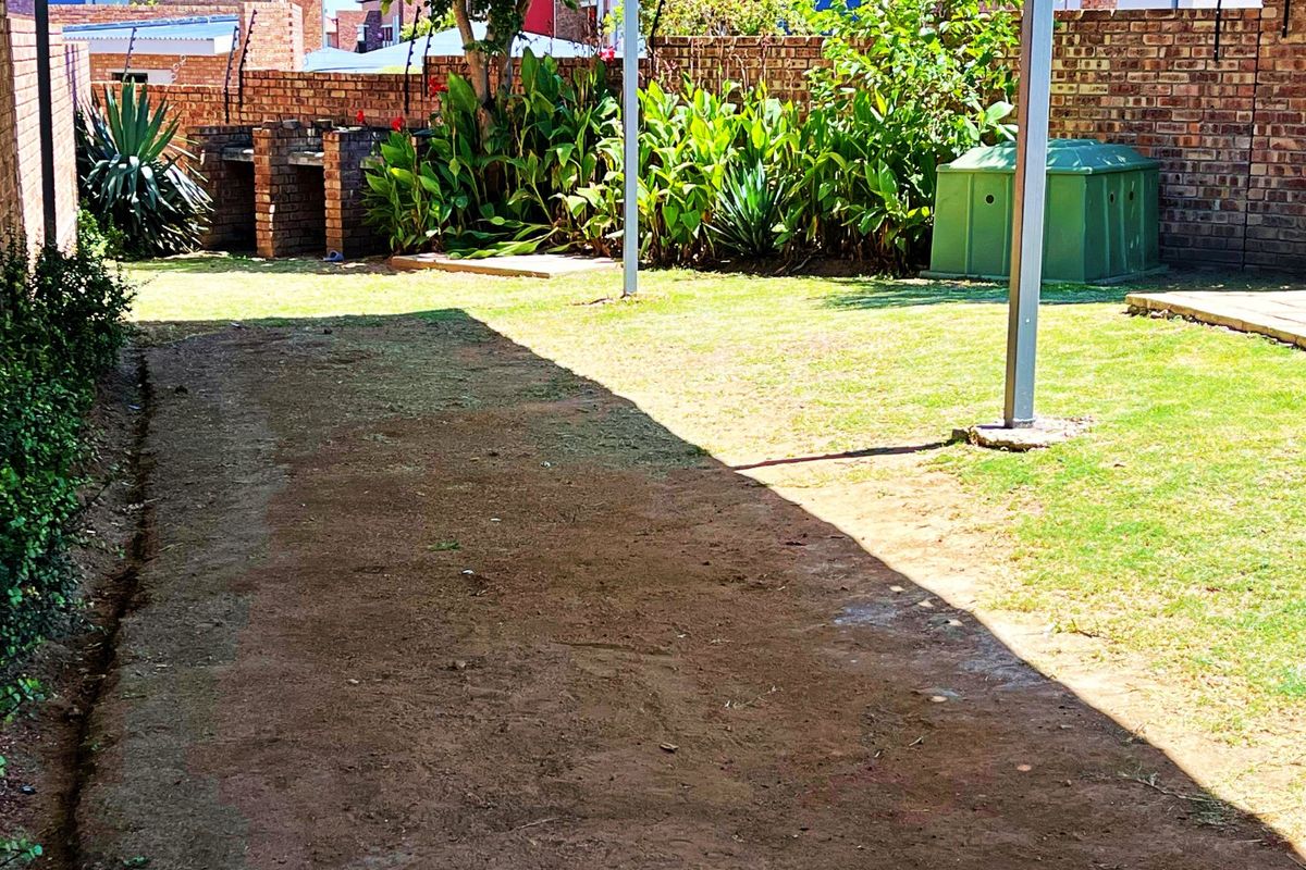 A private rear garden featuring a built-in brick braai, established greenery, and a secure brick boundary wall with electric fencing.