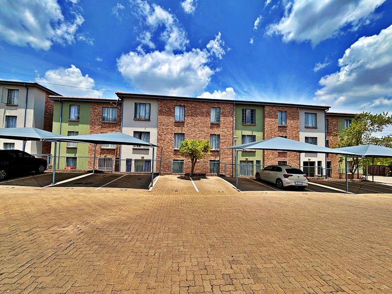 Front exterior view of a multi-story apartment complex featuring brick facade, paved parking area, and covered carports.