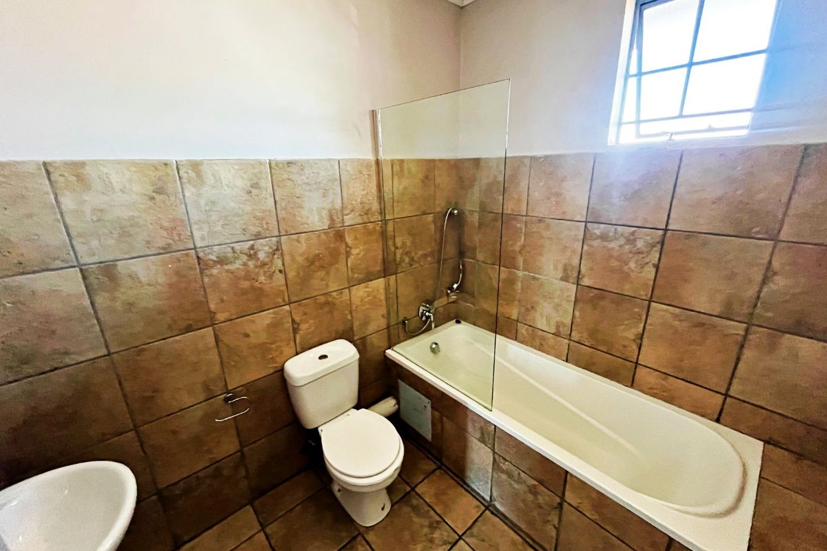 A functional bathroom featuring a bathtub with a glass screen, a toilet, and a wall-mounted basin, finished with neutral ceramic tiling.