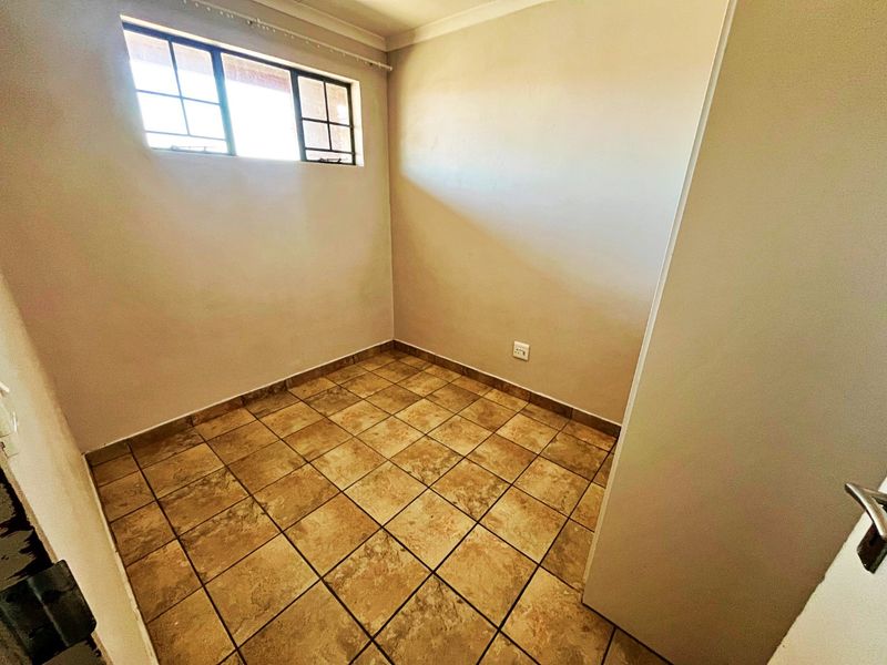 A vacant bedroom featuring neutral wall tones, tiled flooring, and a window providing natural light.