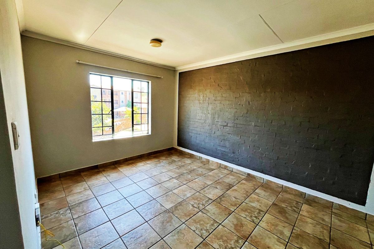An empty bedroom featuring tiled flooring, a dark exposed brick feature wall, and a window fitted with security bars.