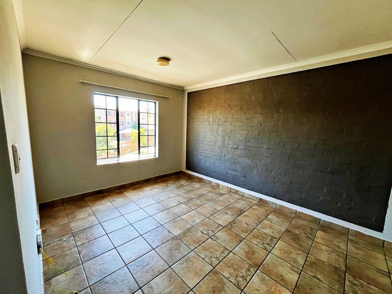 An empty bedroom featuring tiled flooring, a dark exposed brick feature wall, and a window fitted with security bars.