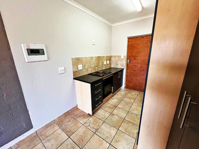 A compact kitchen featuring dark cabinetry, built-in oven and hob, tiled splashback, and tiled flooring, providing a functional and clean workspace.