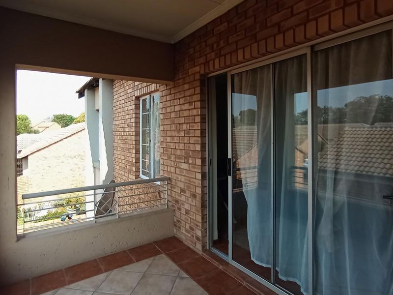 A covered balcony featuring exposed brick walls, tiled flooring, and a metal balustrade, providing an outdoor extension to the living area.
