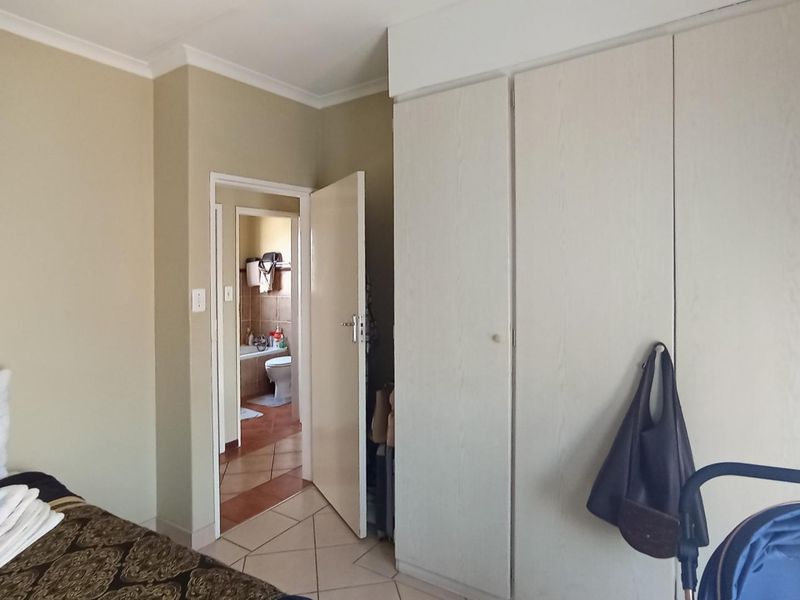 Bedroom featuring built-in cupboards and tiled flooring, with an adjoining bathroom visible through the doorway.