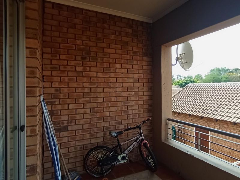 A covered balcony featuring exposed brickwork, tiled flooring, and a stainless steel balustrade, offering an outdoor space for relaxation.