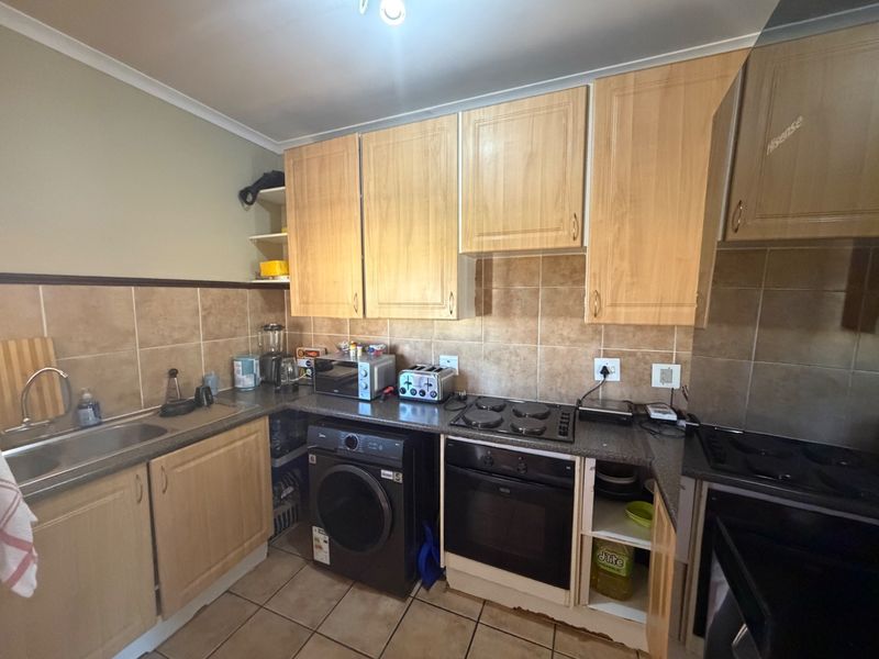 Functional kitchen featuring laminate cabinetry, tiled backsplash, built-in oven, electric hob, and stainless steel sink with tiled flooring.