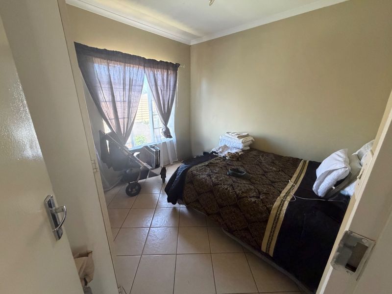 A standard bedroom featuring tiled flooring and a window, providing a functional space with neutral wall tones.