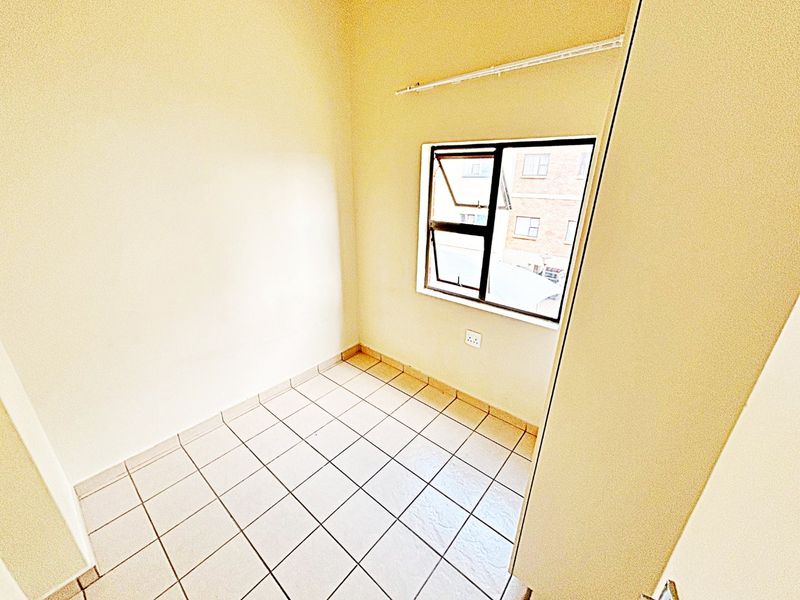 A compact, empty bedroom featuring tiled flooring, a casement window, and a neutral wall finish, ready for personalization.