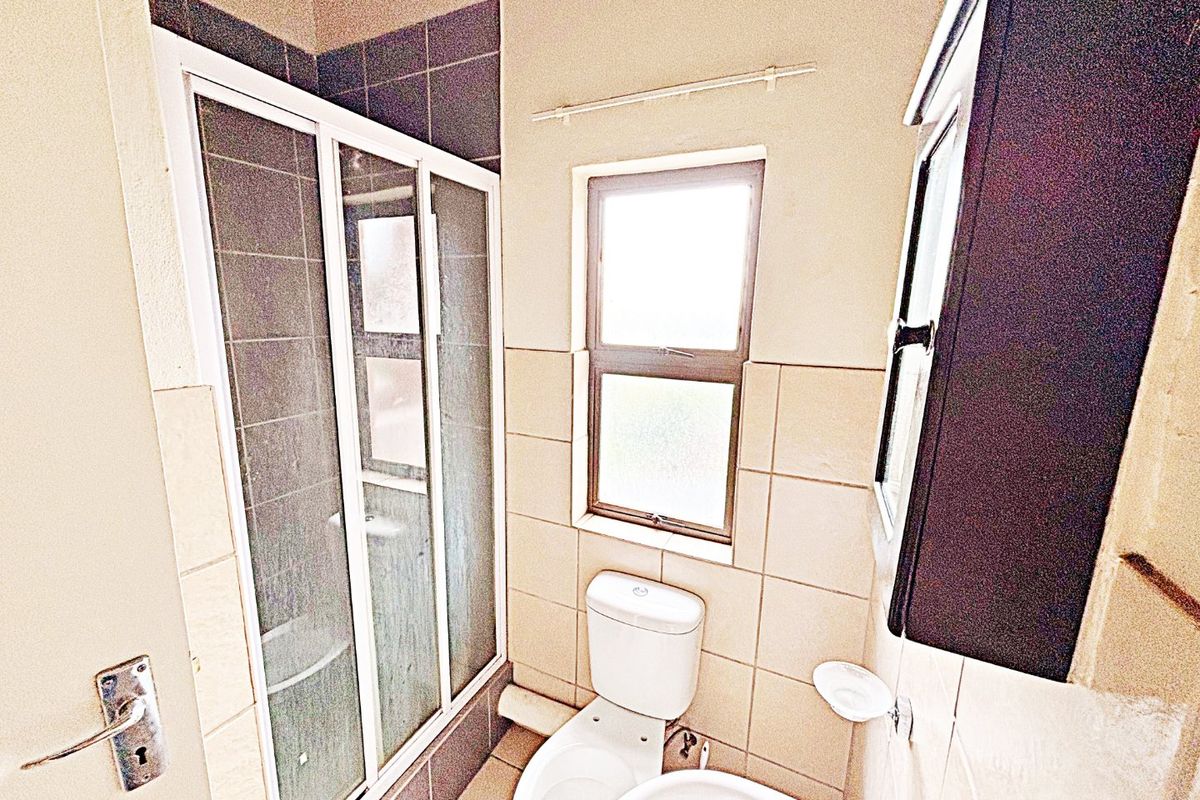 A functional bathroom featuring a shower enclosure, toilet, and basin with neutral wall and floor tiling.