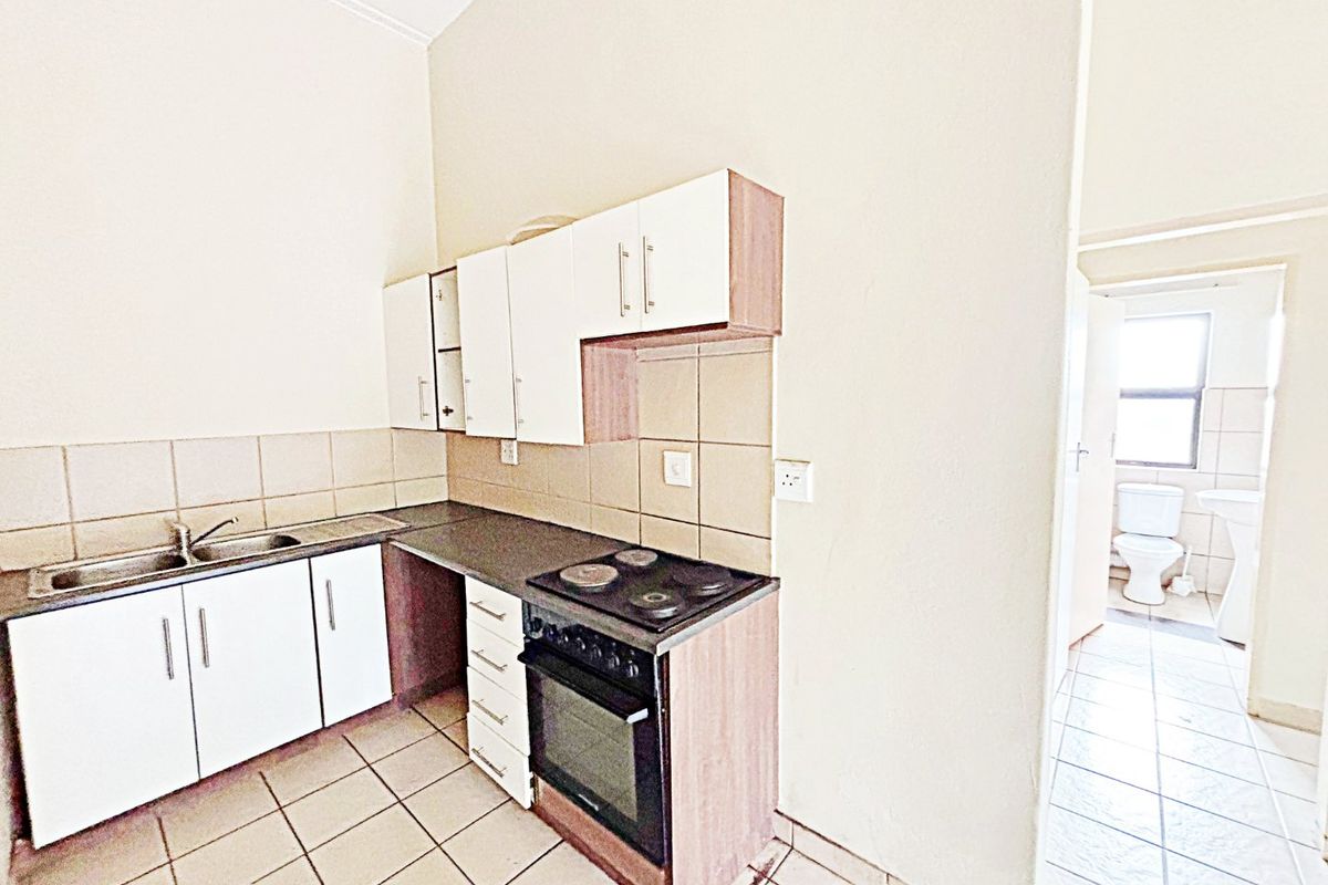 A functional kitchen featuring built-in cabinetry, an electric stove with oven, and tiled flooring, with an adjacent view into a bathroom area.