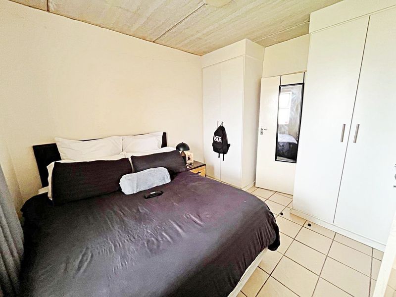 Bedroom featuring built-in cupboards, tiled flooring, and an exposed concrete ceiling. The space offers functional storage and a neutral foundation for updates.