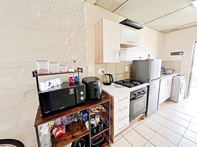 Compact kitchen featuring built-in cabinetry, electric hob, oven, extractor fan, and tiled flooring with an industrial-style exposed concrete ceiling.