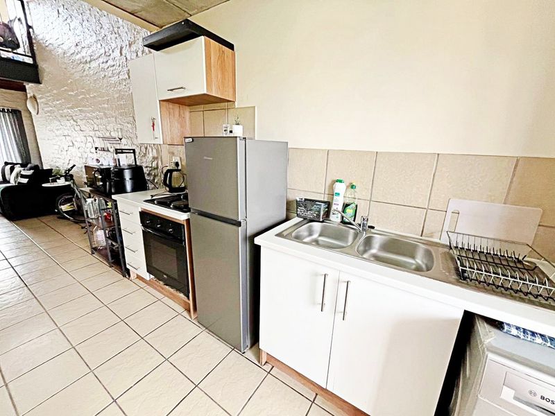 Compact kitchen featuring built-in cabinetry, a double bowl sink, integrated oven and hob, tiled backsplash, and a distinctive exposed brick wall.