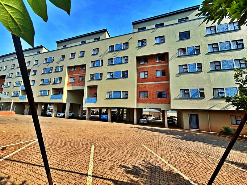 Exterior view of a multi-story apartment building featuring a paved parking area and covered ground-level parking spaces.