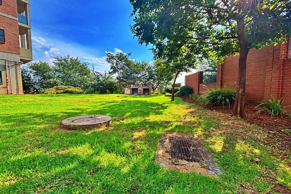 A communal garden area featuring a brick boundary wall, a built-in braai, and established trees, providing outdoor space for residents.