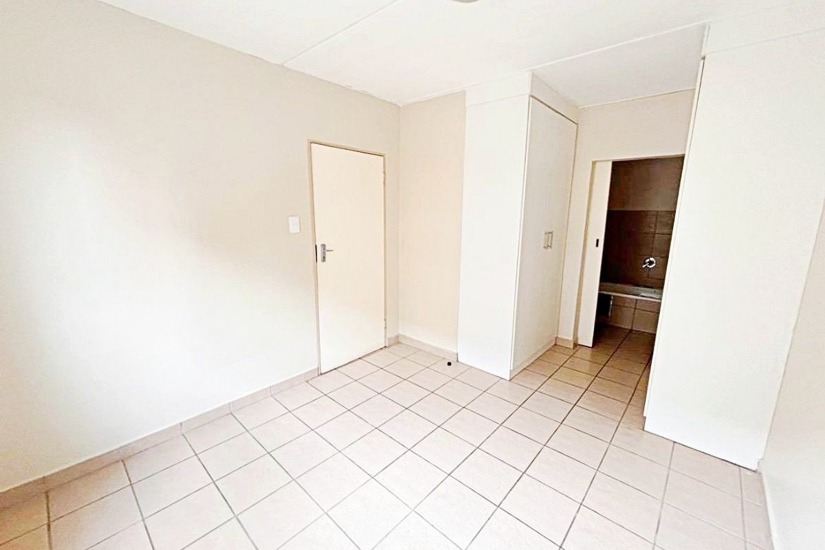 An empty bedroom featuring neutral tiled flooring and built-in cupboards, with direct access to an adjoining bathroom area.