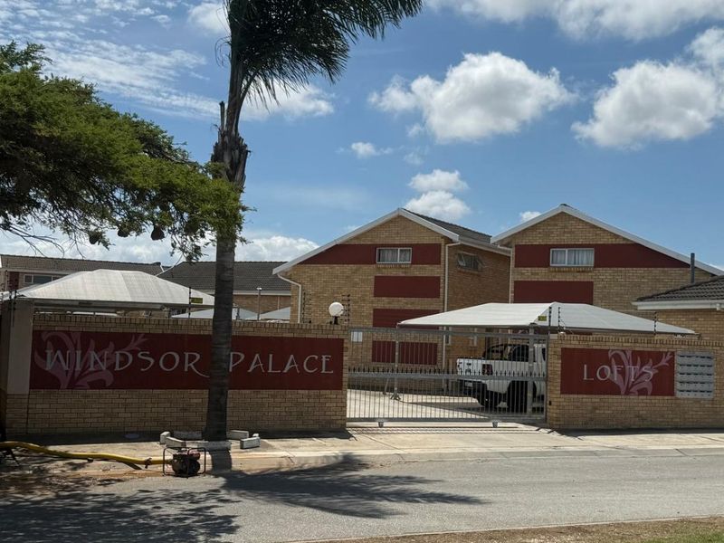 Front entrance view of Windsor Palace Lofts townhouse complex, featuring a brick boundary wall, electric fencing, and secure gated access.