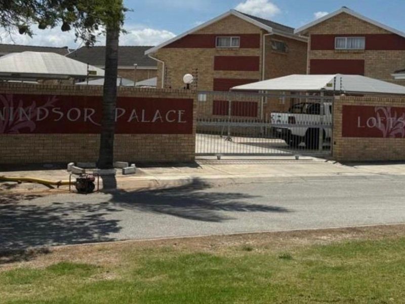 Front entrance view of Windsor Palace Lofts, featuring a brick boundary wall, electric fencing, and a secure gated driveway with carport parking.