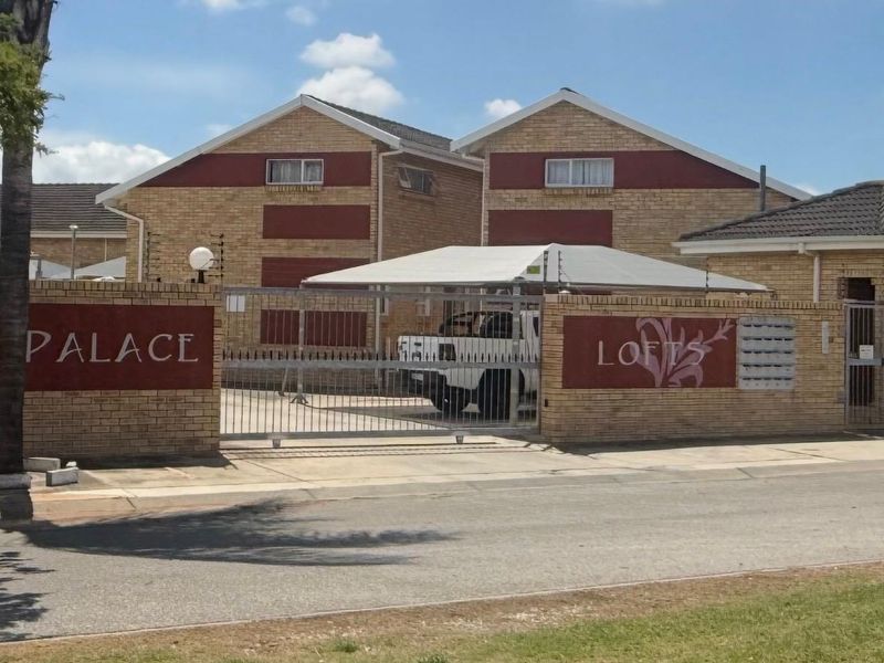 Front view of the Palace Lofts townhouse complex, featuring a secure gated entrance, brick facade, and covered parking area.