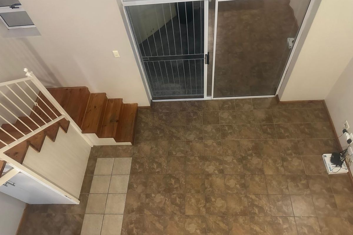 An elevated view of an empty living area featuring tiled flooring, a wooden staircase with a metal balustrade, and sliding glass doors leading outside.