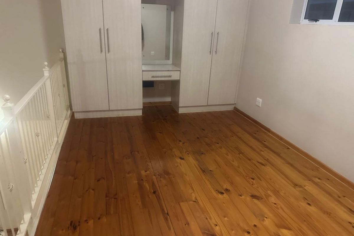 A spacious bedroom featuring polished timber flooring, built-in cupboards with an integrated vanity station, and a protective balustrade overlooking the lower level.