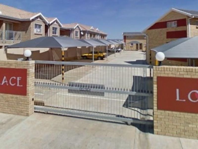 Front entrance view of the Windsor Palace Lofts complex, featuring a secure gated access point, paved driveway, and covered carport parking bays.