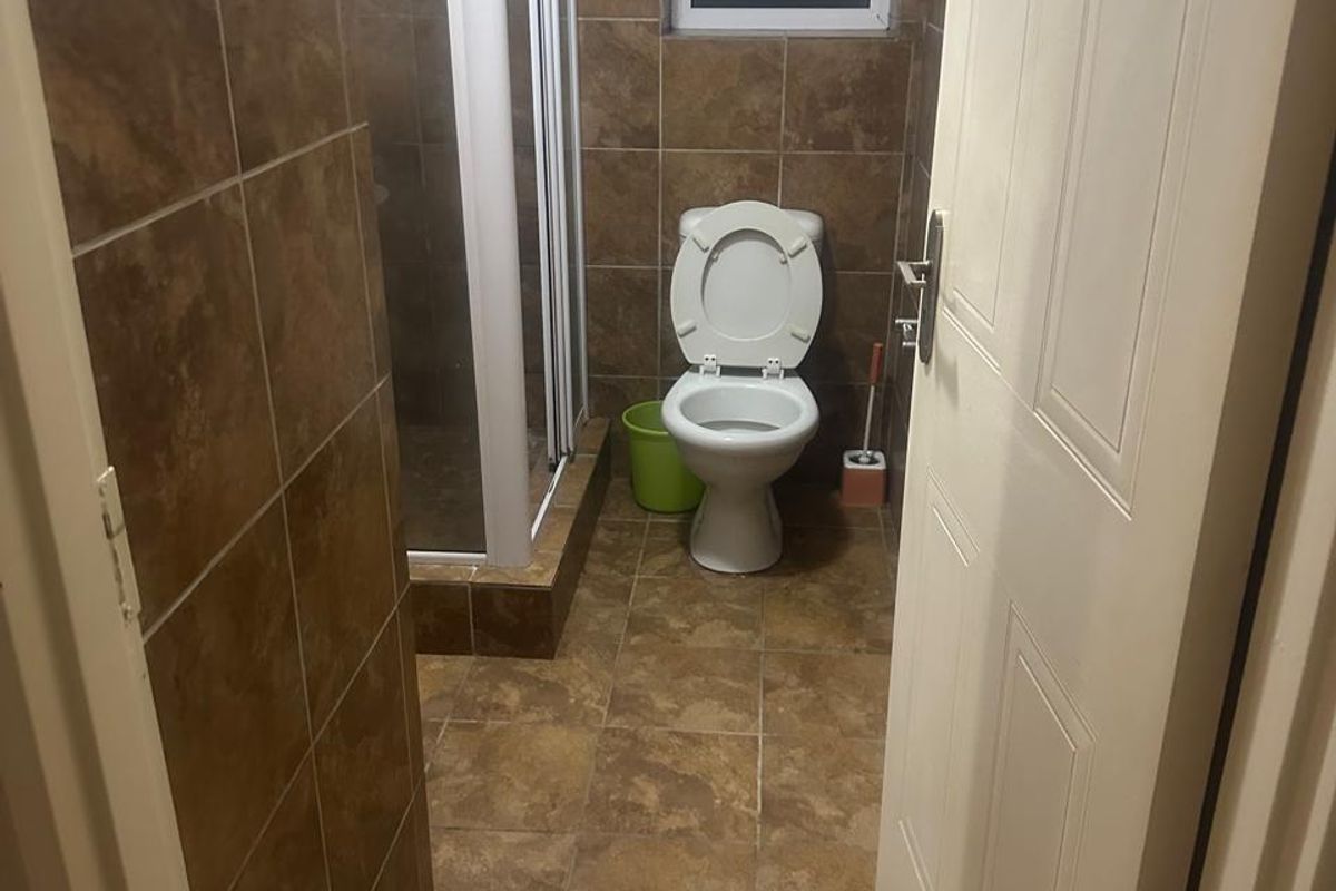 A functional bathroom featuring a shower enclosure, toilet, and full-height brown tiled walls and flooring.