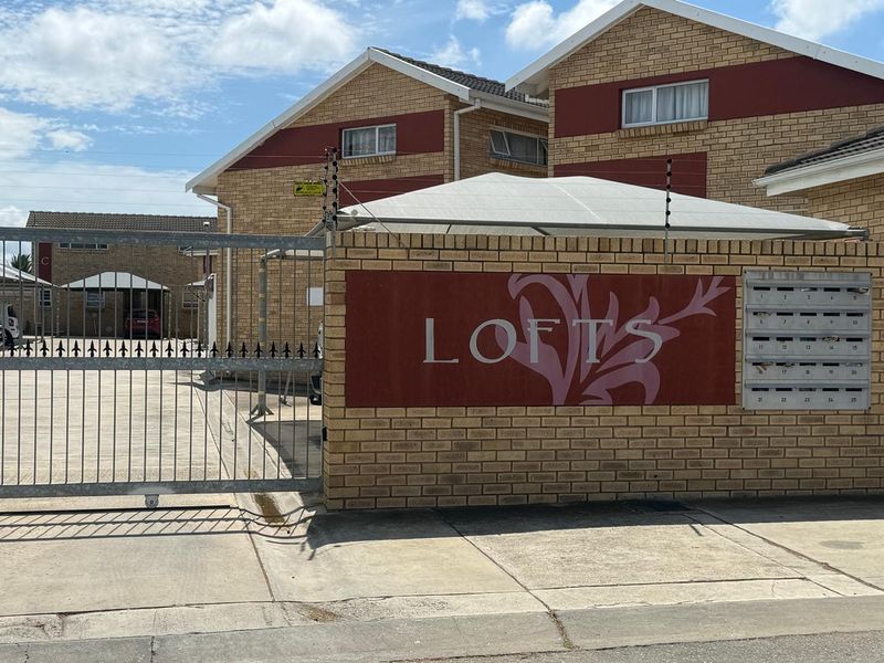Front entrance view of the townhouse complex featuring a brick facade, secure metal gate, electric fencing, and communal post boxes.