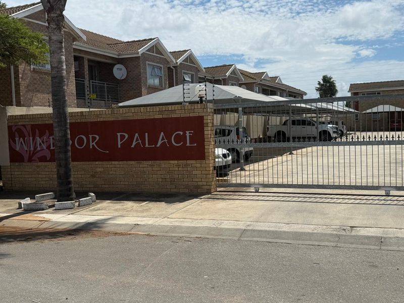 Front entrance view of Windsor Palace townhouse complex featuring a brick boundary wall, secure metal gate, and covered carport parking.