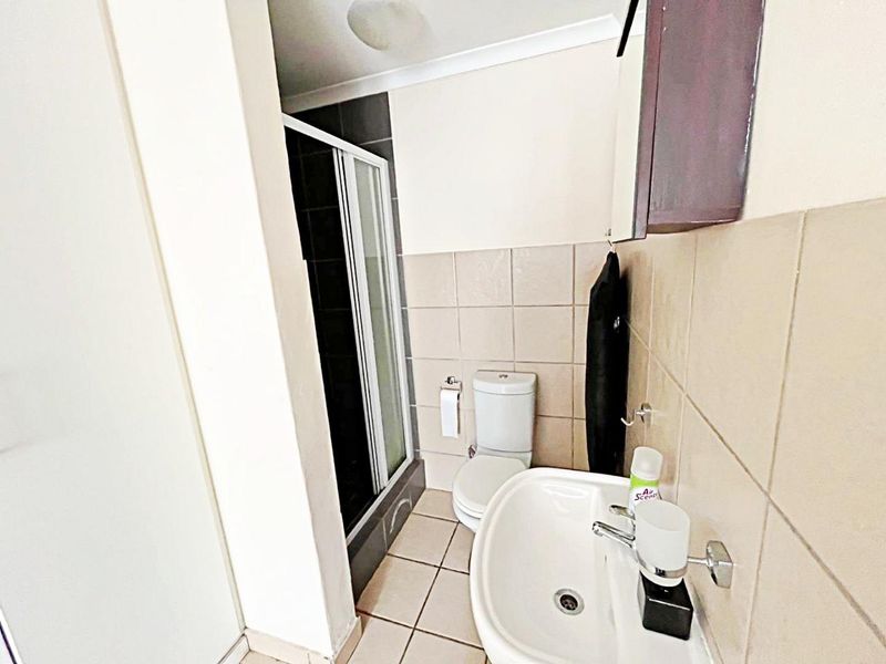 A functional bathroom featuring a shower enclosure, toilet, and washbasin with neutral wall and floor tiling.