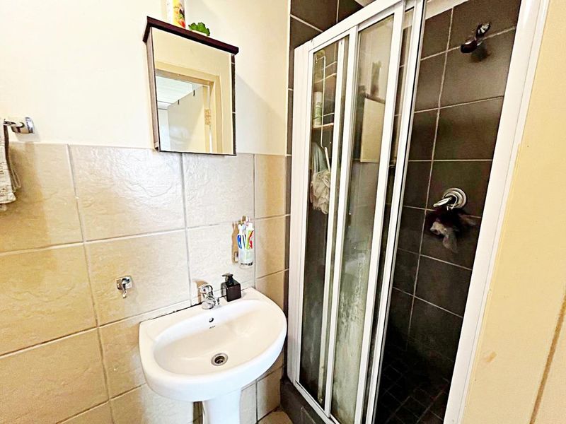 A functional bathroom featuring a pedestal basin, wall tiling, and a shower enclosure with a sliding door.