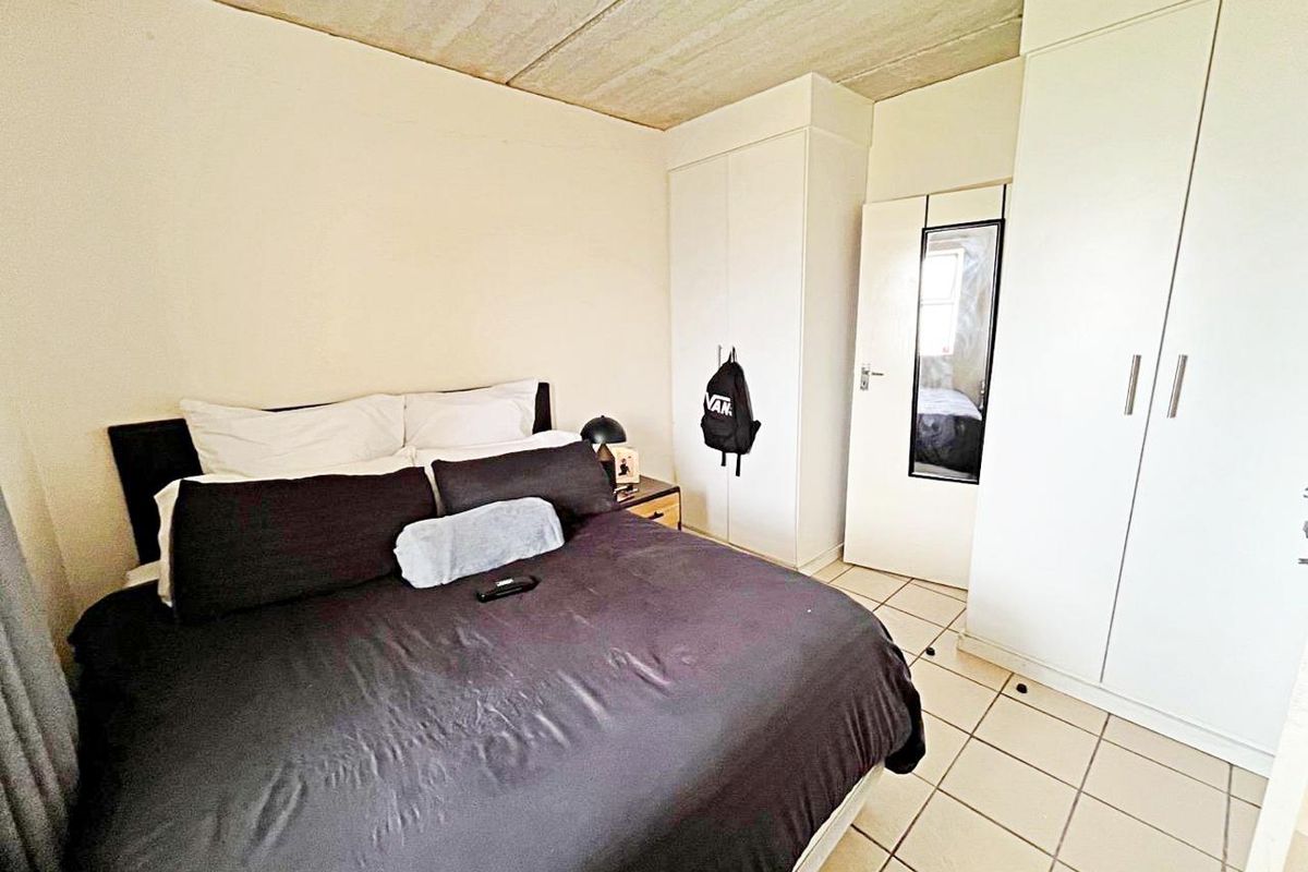 Bedroom featuring built-in cupboards, tiled flooring, and an exposed concrete ceiling.