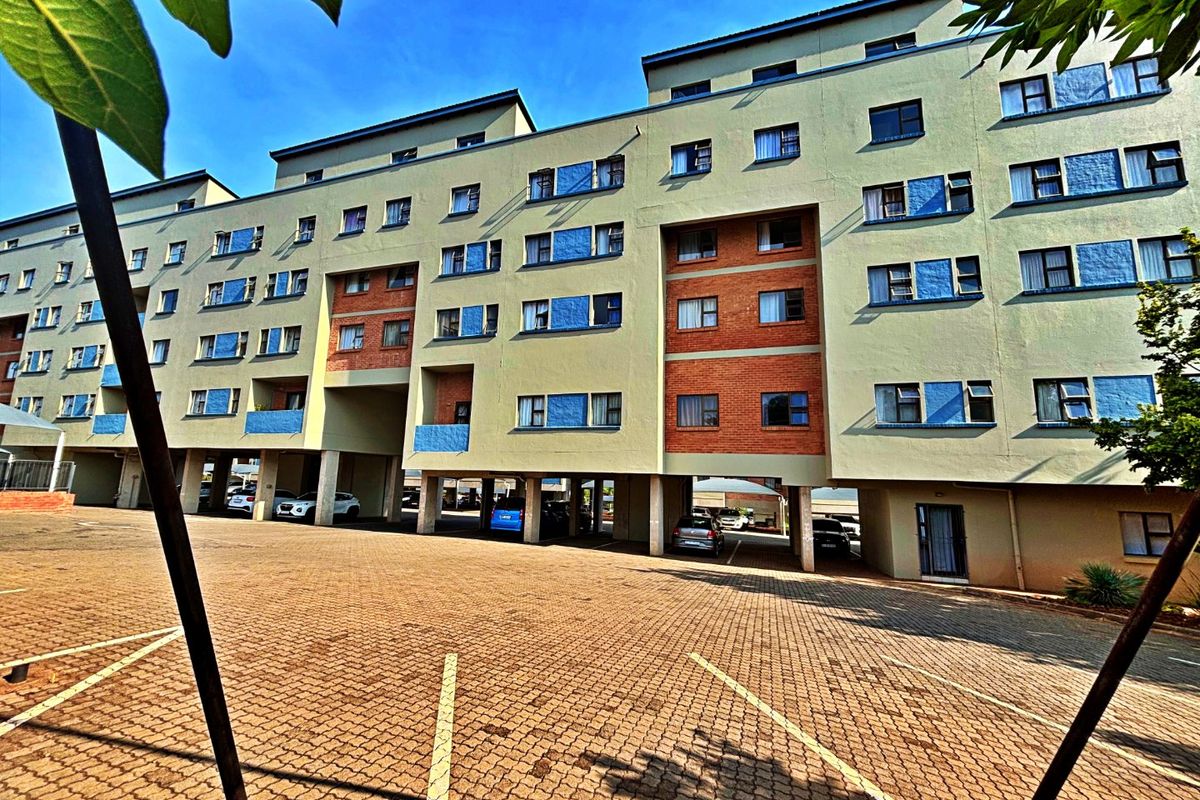 Exterior view of a multi-story apartment building featuring a paved parking area and covered ground-level parking spaces.