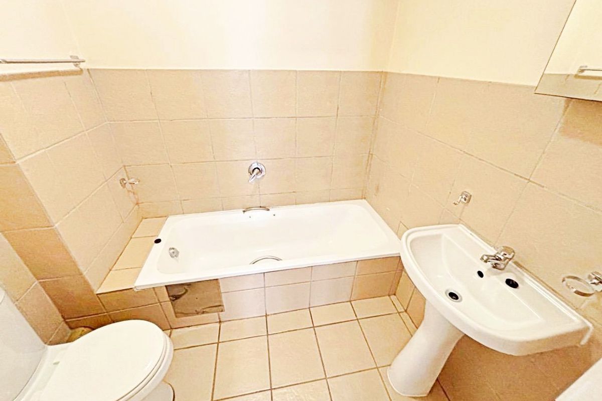 A functional bathroom featuring a bathtub, pedestal basin, and neutral ceramic tiling throughout. The space is ready for cosmetic updates.