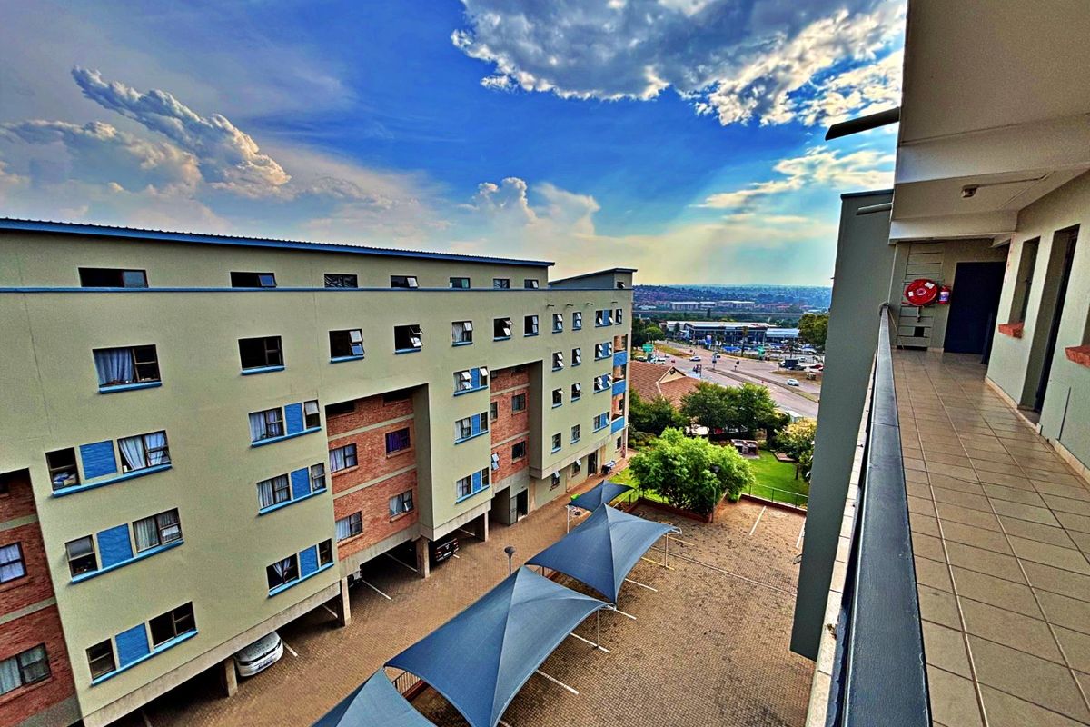 An elevated balcony view overlooking the apartment complex parking area with shade sails and surrounding neighborhood.