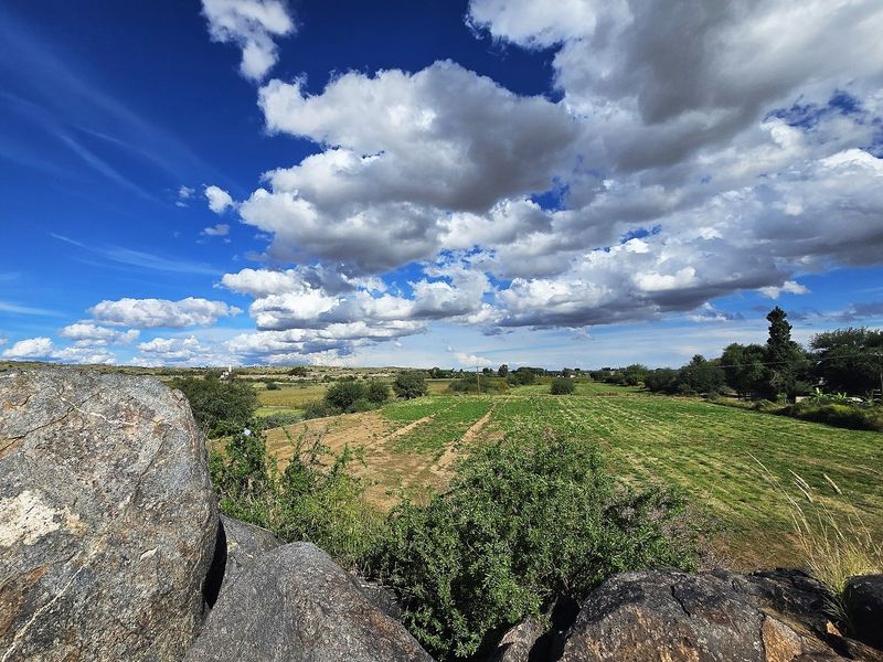 A scenic view overlooking expansive agricultural fields and rural landscape under a bright, cloudy sky.