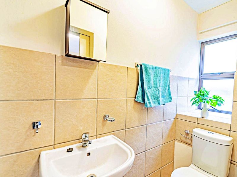 A functional bathroom featuring ceramic wall tiling, a pedestal washbasin with chrome fixtures, a wall-mounted medicine cabinet, and a standard toilet.