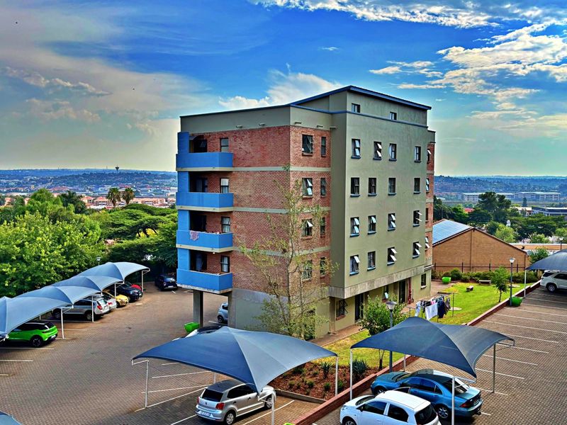 Aerial view of a multi-story apartment building featuring brick and rendered facades, private balconies, and extensive paved parking with shade cloth carports.