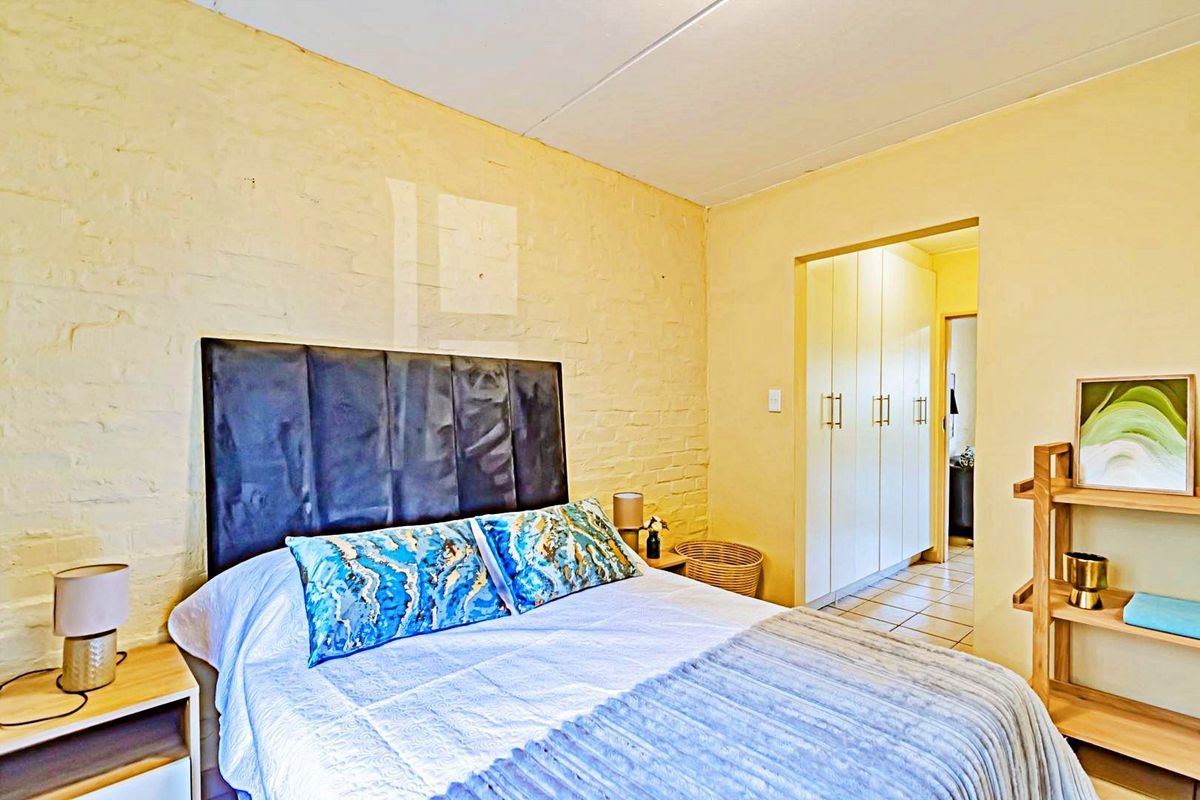 A bedroom featuring an exposed brick wall and built-in cupboards, leading into a tiled hallway area.