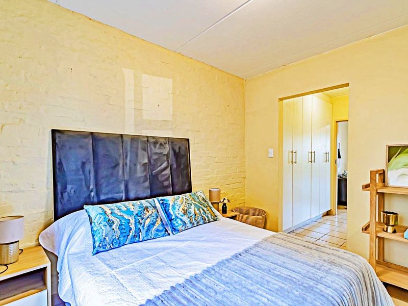 A bedroom featuring an exposed brick wall and built-in cupboards, leading into a tiled hallway area.