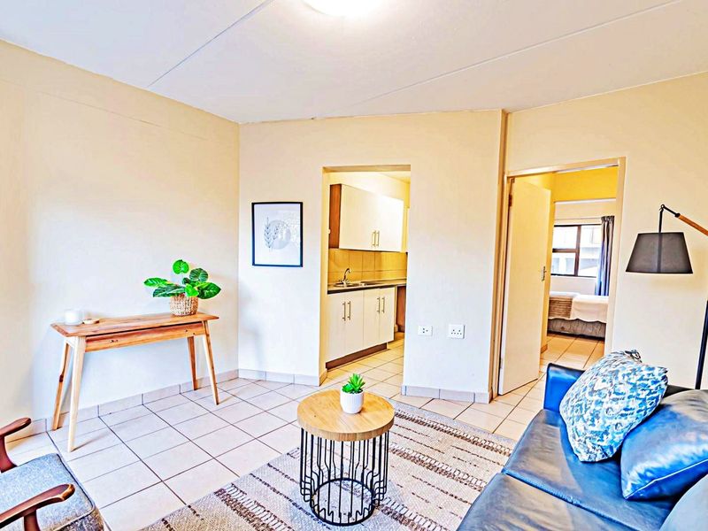 Open plan living area featuring tiled flooring, leading into a compact kitchen space with built-in cabinetry and sink.